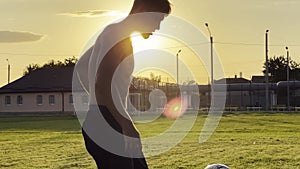 Young man juggling soccer ball on stadium at sunset. Professional footballer kicking ball at green field. Sportsman