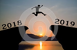 A young man jump between 2018 and 2019 years over the sun and through on the gap of hill silhouette