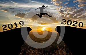 A young man jump between 2019 and 2020 years over the sun and through on the gap of hill silhouette evening colorful sky.