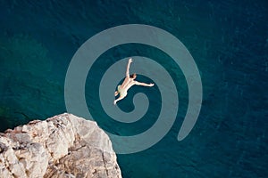 Young man jumping from cliff into sea