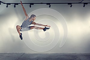 Young man jumping in front of gray wall