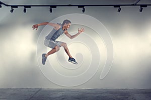 Young man jumping in front of gray wall