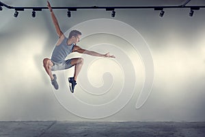 Young man jumping in front of gray wall