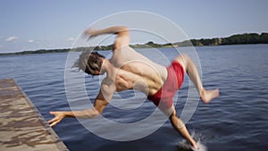 Young man jumping into the lake from wooden pier. Having fun on summer day.