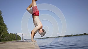 Young man jumping into the lake from wooden pier. Having fun on summer day.