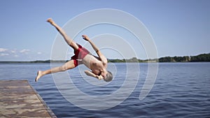 Young man jumping into the lake from wooden pier. Having fun on summer day.