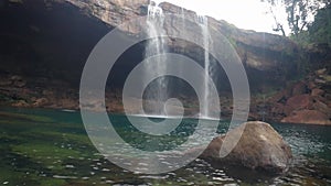 Young man jumping in the natural waterfall falling from mountain top at morning