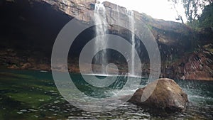 Young man jumping in the natural waterfall falling from mountain top at morning