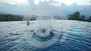 Young man jumping in the pool flips a somersault in slow motion with beautiful clouds infinity sea view in the mountain