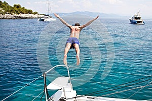 Young man jumping from a sailing boat.