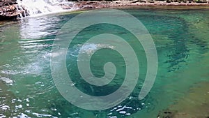 Young man jumping and swimming in blue clear water of waterfall from flat angle