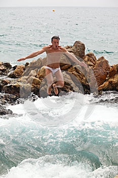 Young man jumping into water from pile of rocks