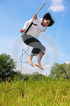 Young man jumps with guitar on grass