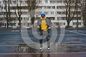 Young man jumps in puddle on sports stadium on background of high-rise building. Happy guy with blue hair having fun on