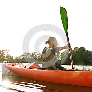 Young man kayaking on river, holding paddle, looking away on a summer day