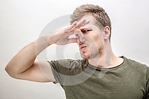 Young man keeps nose closed. He smells bad smell. Isolated on white background.