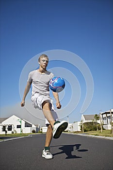 Young Man Kicking Ball On Street