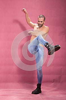 Young man kicking boots, pink background, shirtless