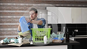 Young man in kitchen during quarantine. Guy sorting plastic bottles and packages with bags. Put them into green basket