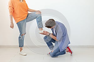 Young man is kneeling and reverently tying shoelaces to his domineering unidentified woman posing on a white background