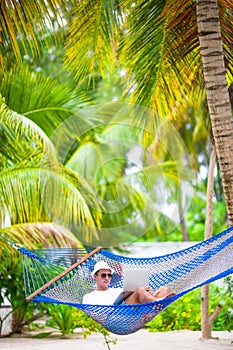 Young man with laptop at hammock on tropical vacation