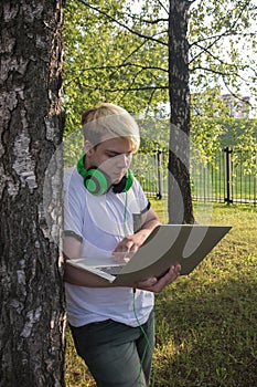 Young man with laptop and headphones working in the park near office building