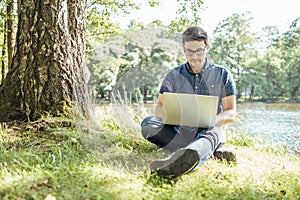 Young man with laptop outdoor sitting on the grass