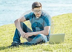 Young man with laptop outdoor sitting on the grass