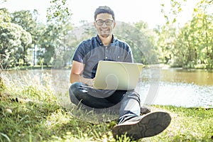 Young man with laptop outdoor sitting on the grass