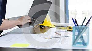 Young man with a laptop plotting a system of building structures in blueprints