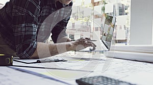 Young man with a laptop plotting a system of building structures in blueprints