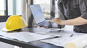 Young man with a laptop plotting a system of building structures in blueprints