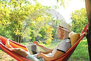 Young man with laptop resting in comfortable hammock at garden