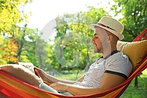 Young man with laptop resting in hammock at green garden