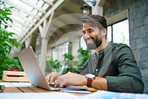 Young man with laptop sitting indoors in green office, working.