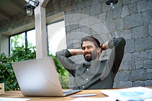 Young man with laptop sitting indoors in office, working.