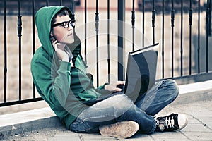 Young man with laptop sitting on sidewalk