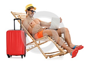 Young man with laptop and suitcase on sun lounger against white background