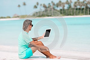 Young man with laptop at tropical beach near water villa