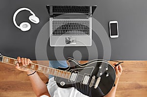 Young man with laptop tuning guitar at table