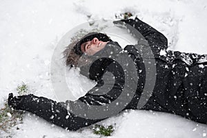 Young man laughing, with happy expression, snow covered, lying on the ground in snowfall.