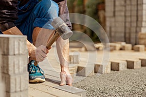 Young man laying gray concrete paving slabs in house courtyard on gravel foundation base. Master lays paving stones