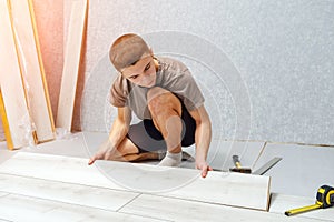 Young man is laying wooden panel of laminate floor indoors.