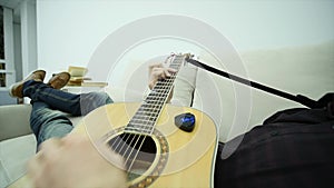 The young man lays on the couch and plays the guitar