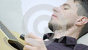 The young man lays on the couch and plays the guitar