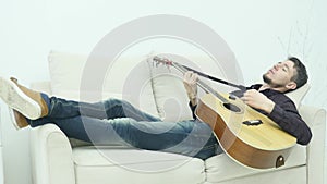 The young man lays on the couch and plays the guitar