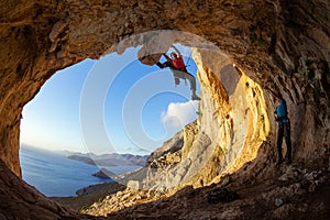 Young man lead climbing on ceiling in cave, another belaying