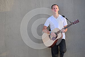 Young man leaning against wall playing acoustic guitar