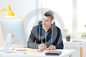 Young man learning at the desk, listening the music and writing