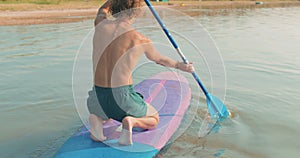 Young man learning to paddle on sup board with paddle.